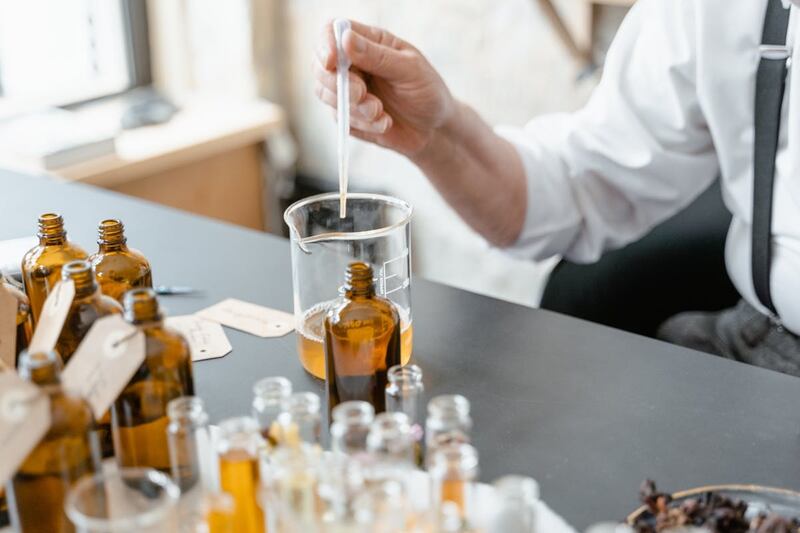 hombre haciendo pruebas en laboratorio de perfumería, frascos de vidrio, pipetas